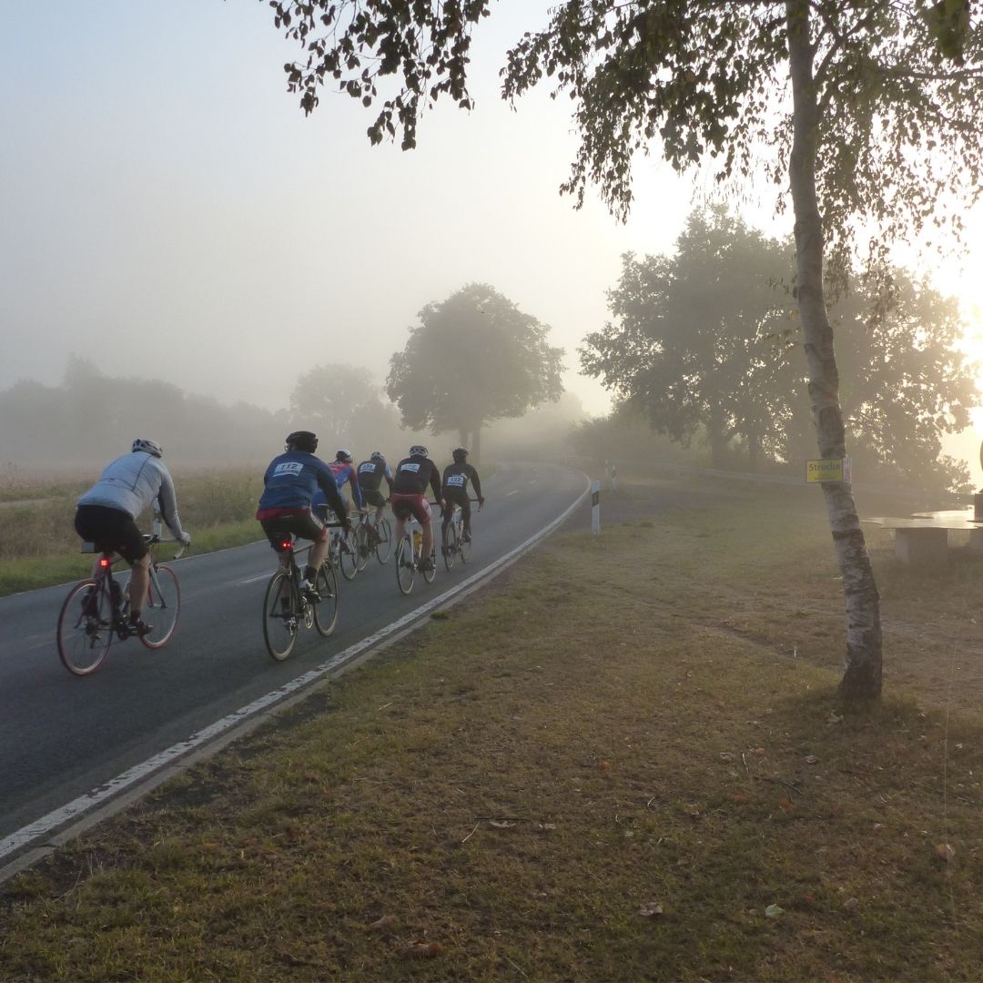Teilnehmende der Großen Weserrunde fahren auf einer Landstraße durch den Morgennebel des Weserberglands.