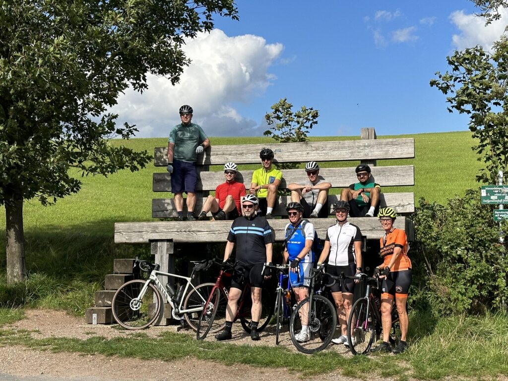 Teilnehmende der Großen Weserrunde legen an der großen Sitzbank in Wennenkamp eine Pause ein.