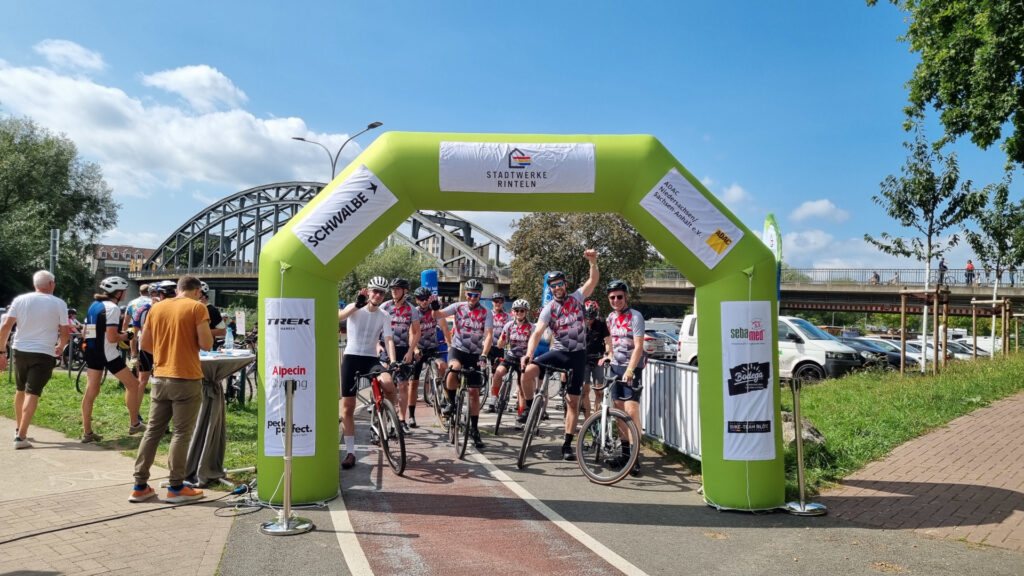 Teilnehmende der Großen Weserrunde versammeln sich unter dem Startbogen am Weseranger in Rinteln vor dem Beginn der Tour.