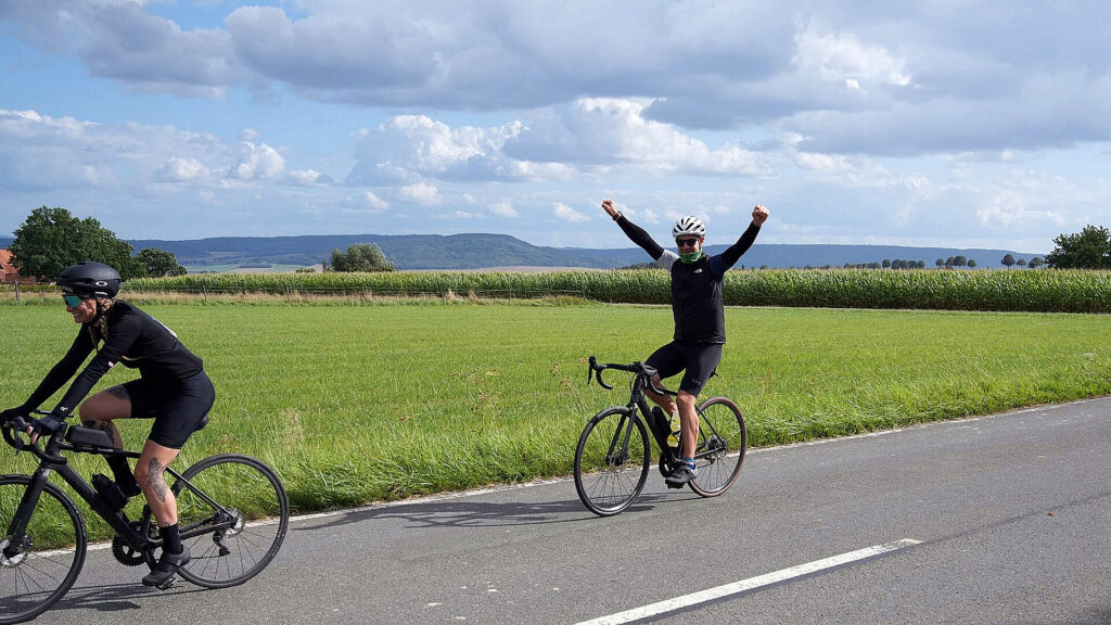 Zwei Teilnehmende der Großen Weserrunde fahren auf einer Landstraße durch die Landschaft des Weserberglands.
